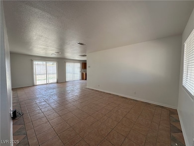Tiled empty room with a textured ceiling and baseb