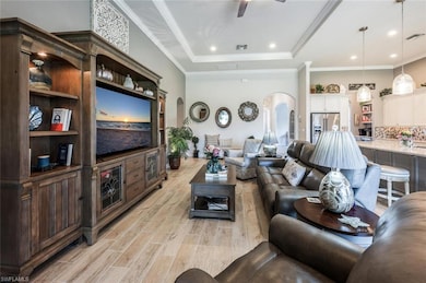Living room featuring arched walkways, light wood-style floors, a raised ceiling, and ceiling fan
