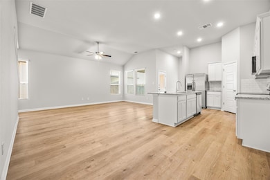 Kitchen with tasteful backsplash, open floor plan, light wood finished floors, a center island with sink, and vaulted ceiling