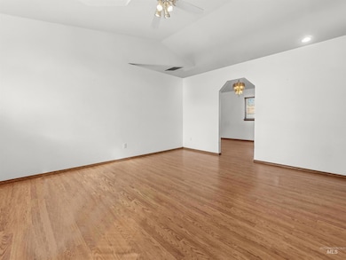 Empty room featuring arched walkways, light wood-style flooring, lofted ceiling, and ceiling fan