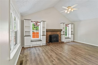 Unfurnished living room featuring ceiling fan, a fireplace, light wood-style flooring, high vaulted ceiling, and a textured ceiling
