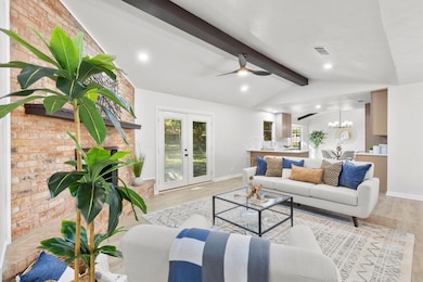 Living room with a chandelier, french doors, wood finished floors, brick wall, and recessed lighting