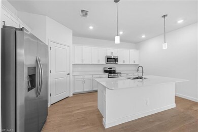 Kitchen with stainless steel appliances, a sink, light wood-style floors, white cabinets, and light countertops