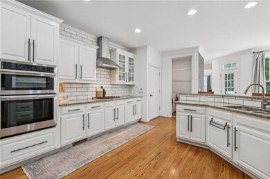Kitchen featuring wall chimney range hood, appliances with stainless steel finishes, recessed lighting, white cabinets, and decorative backsplash