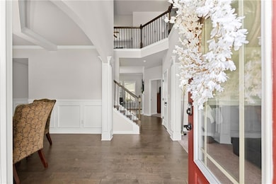 Entrance foyer with stairway, dark wood finished floors, a towering ceiling, ornate columns, and arched walkways