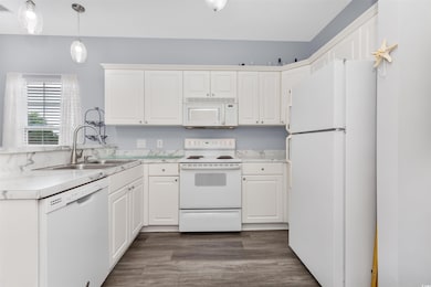 Kitchen featuring white appliances, a sink, white cabinetry, light countertops, and dark wood finished floors