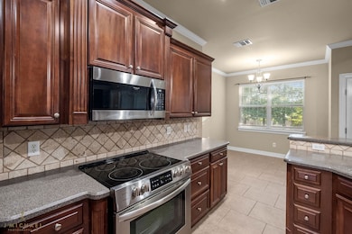 Kitchen featuring appliances with stainless steel finishes, crown molding, backsplash, light tile patterned floors, and a chandelier