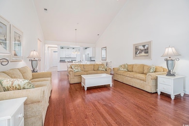 Living area with high vaulted ceiling, wood finished floors, and a chandelier