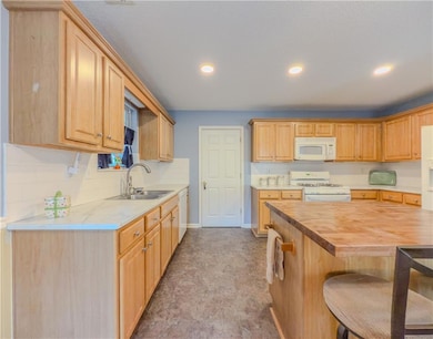 Kitchen featuring white appliances, recessed lighting, a breakfast bar area, backsplash, and butcher block counters