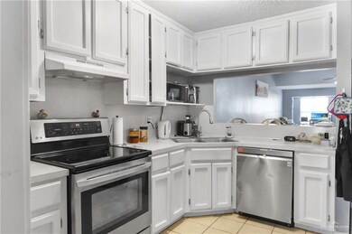 Kitchen with stainless steel appliances, white cabinetry, light countertops, light tile patterned floors, and under cabinet range hood