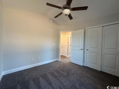 Unfurnished bedroom featuring lofted ceiling, a closet, dark carpet, ceiling fan, and baseboards