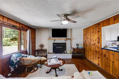 Living area featuring wooden walls, wood finished floors, ceiling fan, a textured ceiling, and a fireplace