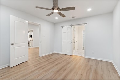 Empty room featuring a barn door, ceiling fan, and light wood-type flooring
