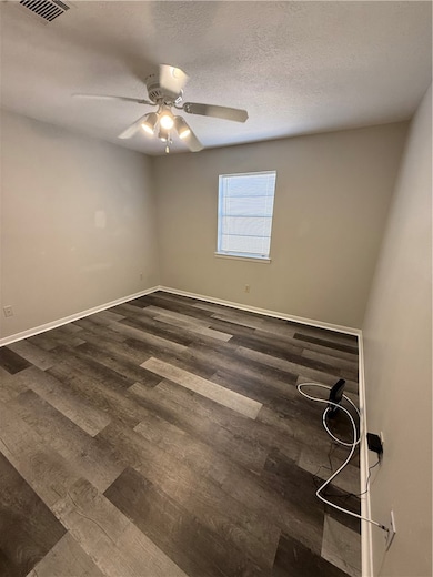 Spare room featuring a textured ceiling, dark wood-type flooring, and ceiling fan