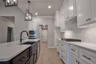Kitchen featuring light stone counters, appliances with stainless steel finishes, light wood-type flooring, white cabinetry, and pendant lighting