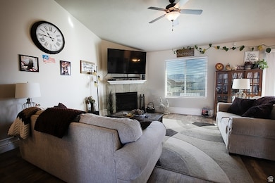 Living area with vaulted ceiling, a tiled fireplace, wood finished floors, and ceiling fan