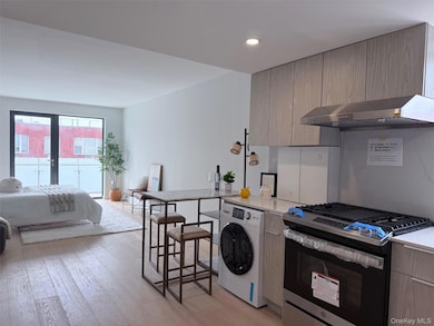 Kitchen with stainless steel gas range oven, washer / dryer, exhaust hood, modern cabinets, and light wood finished floors