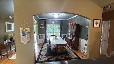 Dining room with arched walkways, ornamental molding, wood finished floors, a wainscoted wall, and a decorative wall