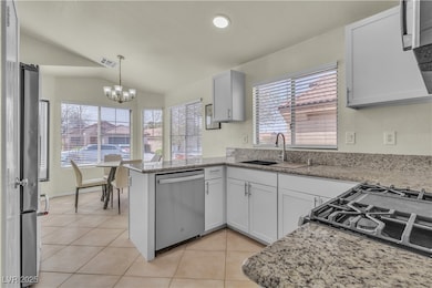 Kitchen featuring a peninsula, lofted ceiling, light tile patterned floors, stainless steel appliances, and hanging light fixtures