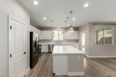 Kitchen with pendant lighting, stainless steel appliances, white cabinetry, light wood-style floors, and recessed lighting