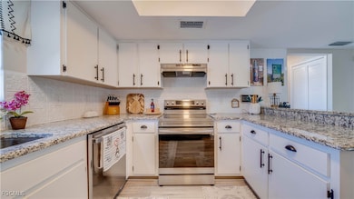 Kitchen featuring appliances with stainless steel finishes, white cabinetry, decorative backsplash, and granite counters