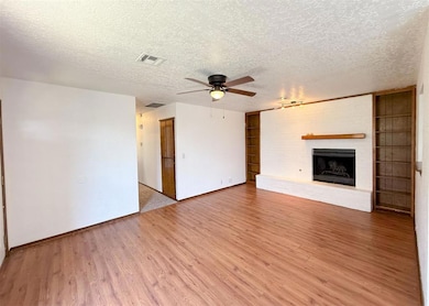 Unfurnished living room featuring light wood-style flooring, a brick fireplace, a ceiling fan, and a textured ceiling