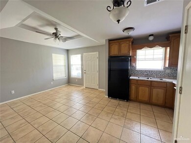 Kitchen with freestanding refrigerator, light countertops, light tile patterned flooring, brown cabinets, and a ceiling fan