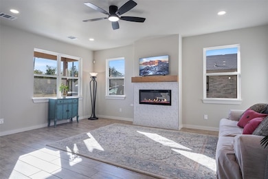 Living area with light wood-style flooring, a glass covered fireplace, recessed lighting, and a ceiling fan