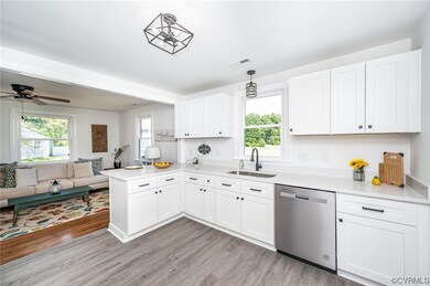 Kitchen with decorative light fixtures, stainless steel dishwasher, light countertops, light hardwood floors, and white cabinetry