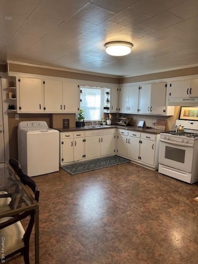 Kitchen featuring dark countertops, stove, washer / clothes dryer, white cabinetry, and ornamental molding