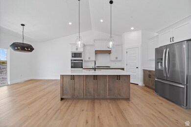 Kitchen with stainless steel appliances, white cabinets, lofted ceiling, brown cabinets, and hanging light fixtures