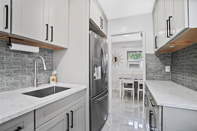 Kitchen featuring backsplash, stainless steel fridge with ice dispenser, light stone counters, and gray cabinetry
