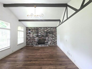 Unfurnished living room with a brick fireplace, wood finished floors, baseboards, and a chandelier