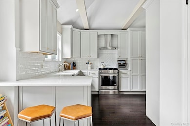 Kitchen featuring decorative backsplash, gas stove, a kitchen bar, wall chimney range hood, and light stone counters