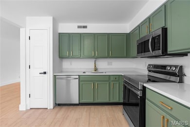 Kitchen with green cabinetry, appliances with stainless steel finishes, light wood-style floors, and light stone counters