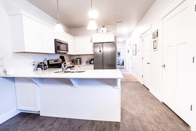 Kitchen featuring appliances with stainless steel finishes, a peninsula, wood finished floors, a breakfast bar area, and light countertops