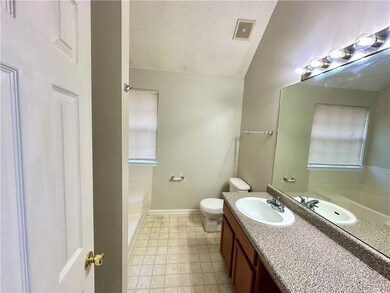 Bathroom featuring a textured ceiling, a garden tub, vanity, toilet, and baseboards