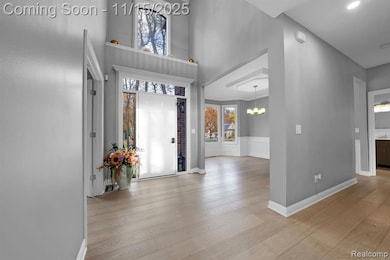 Foyer with a chandelier, light wood-style floors, a high ceiling, and a wainscoted wall