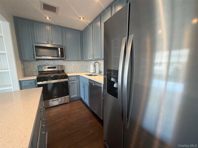Kitchen with stainless steel appliances, decorative backsplash, light stone counters, dark wood-style floors, and recessed lighting