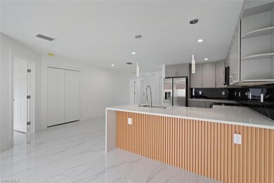 Kitchen with open shelves, gray cabinetry, light stone counters, decorative light fixtures, and stainless steel refrigerator with ice dispenser