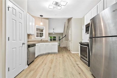 Kitchen featuring appliances with stainless steel finishes, white cabinets, light wood finished floors, light countertops, and decorative light fixtures