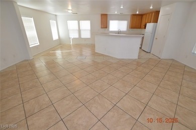 Kitchen featuring open floor plan, freestanding refrigerator, brown cabinets, light tile patterned floors, and light countertops