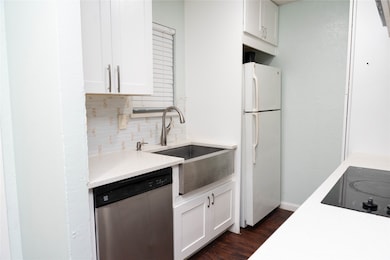 Kitchen featuring stainless steel dishwasher, freestanding refrigerator, tasteful backsplash, and white cabinets
