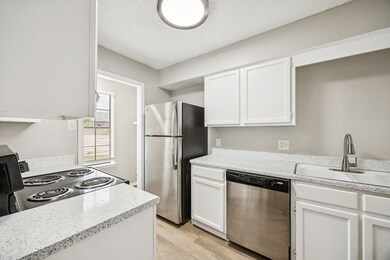 Kitchen featuring appliances with stainless steel finishes, a textured ceiling, white cabinets, light wood-style flooring, and light stone countertops