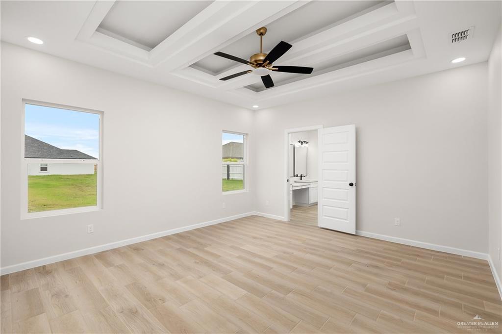 Spare room with a tray ceiling, light wood-type flooring, and ceiling fan