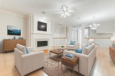 Expansive and light-filled, the second-floor living area features gleaming hardwood floors, elegant crown molding, and a gaslog fireplace framed by custom millwork and decorative wall paneling. Multiple windows with plantation shutters invite natural light while maintaining privacy. This open-concept space seamlessly blends style and comfort.