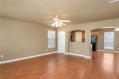 Unfurnished living room featuring arched walkways, light wood-type flooring, ceiling fan, and a textured ceiling