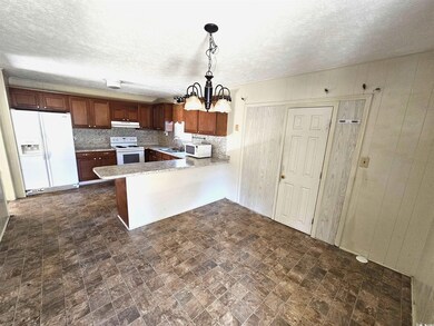 Kitchen with white appliances, a peninsula, an inviting chandelier, hanging light fixtures, and wood walls