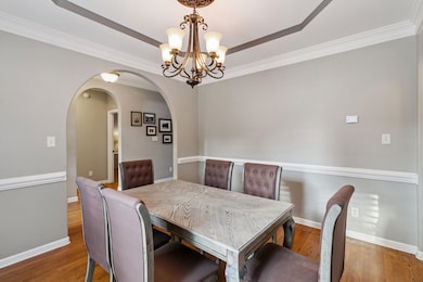 Dining area with a chandelier, ornamental molding, wood finished floors, arched walkways, and a raised ceiling