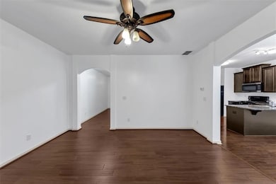 Unfurnished living room featuring arched walkways, a ceiling fan, and dark wood finished floors
